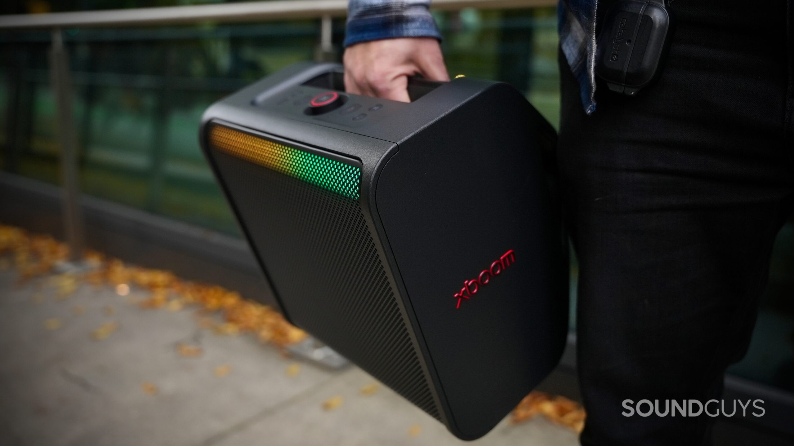 LG xboom Stage 301 - 2 A hand holding the LG xboom Stage 301 by its handle in an outdoor setting.